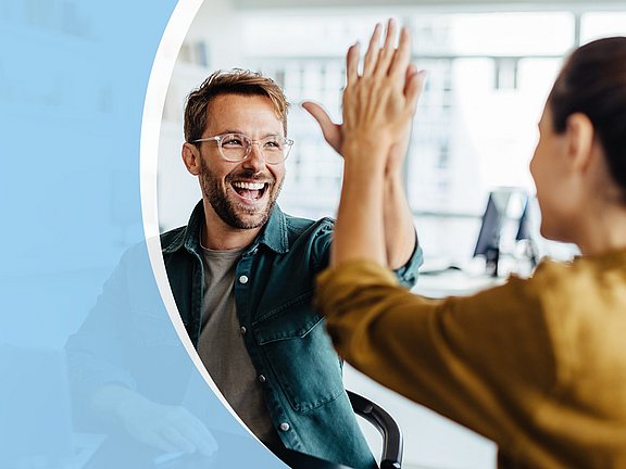 Zwei lächelnde Menschen, die sich in einer hellen Büroumgebung ein High Five geben, mit einer blauen Überlagerung auf der linken Seite.